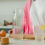A woman in a pink outfit prepares lemon water in a bright, modern kitchen setting.